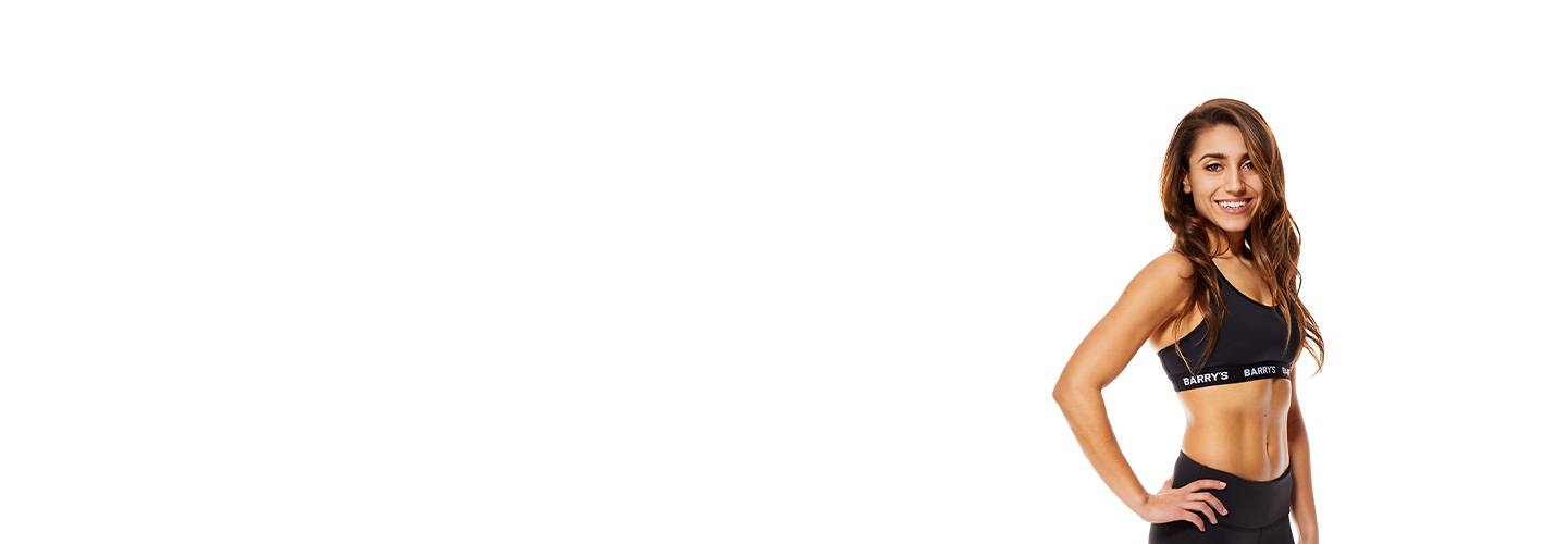 Instructor Amanda Asaro in black Barry's Bootcamp sports bra with hand on hip smiling on white background