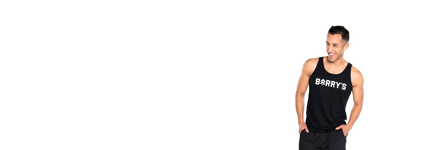 Instructor Andrew Nunez in black Barry's Bootcamp tank top with hands in shorts pockets smiling on white background