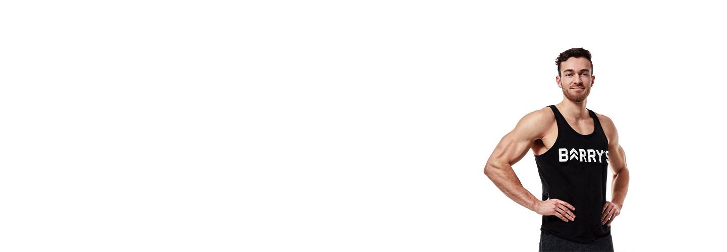 Instructor Austin Cagley in black Barry's Bootcamp tank top smiling with hands on hips on white background