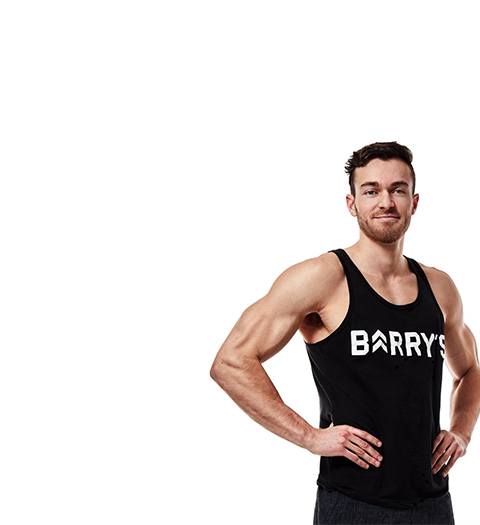 Instructor Austin Cagley in black Barry's Bootcamp tank top smiling with hands on hips on white background