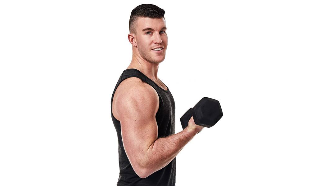 Barry's Bootcamp instructor Connor Miller in black tank top smiling while doing bicep curl with dumbbell on white background