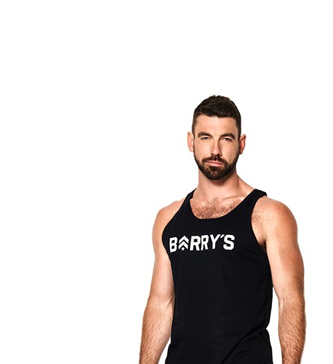 Barry's Bootcamp instructor Cory Gooch standing against a white background wearing a tank top with a Barry's logo.