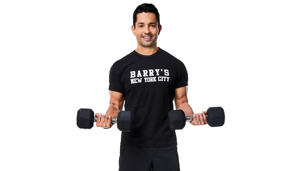Instructor Harley Rodriguez in a Black Barry's T shirt curling dumbbells