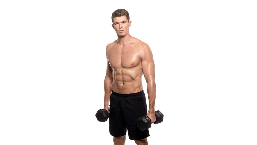 Barry's Bootcamp instructor Harry Sellers shirtless holding two dumbbells against a white background.