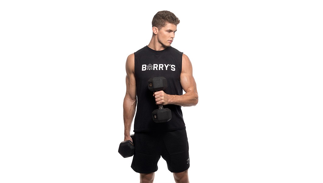Barry's Bootcamp instructor Harry Sellers wearing a black Barry's tank top holding dumbbells.