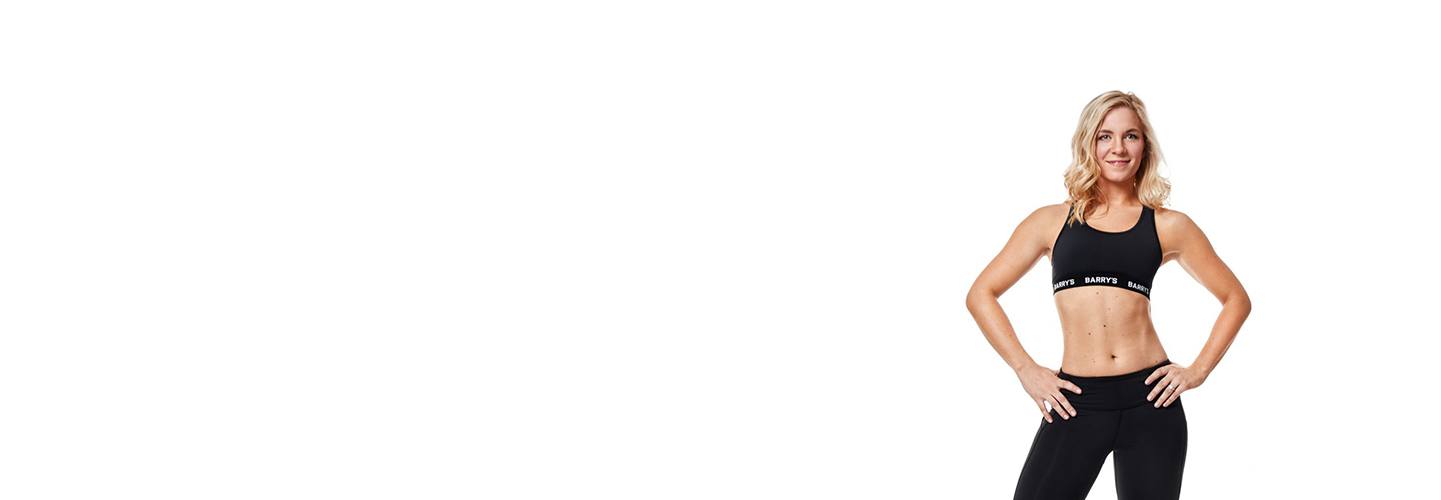 Instructor Jenna (Mazanowksi) Miller in black Barry's Bootcamp sports bra smiling with hands on hips on white background