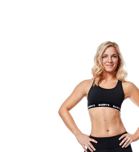 Instructor Jenna (Mazanowksi) Miller in black Barry's Bootcamp sports bra smiling with hands on hips on white background