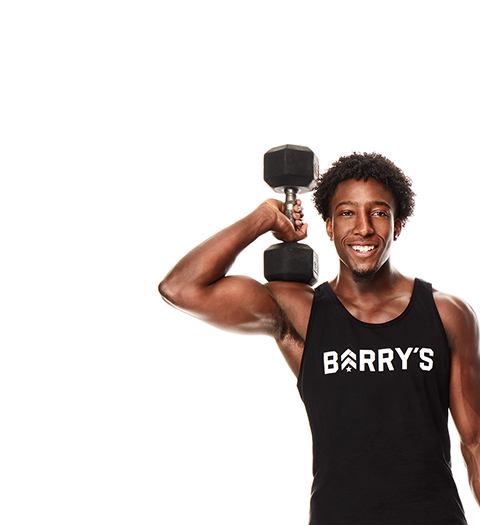 Barry's Bootcamp instructor Joseph Allen wearing a black tank top with a Barry's logo on it holding a dumbbell up near his shoulder.