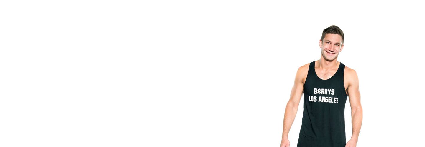 المدرب جوردان غلوك يرتدي الجزء العلوي من دبابة Barry's Bootcamp باللون الأسود ويبتسم على خلفية بيضاء