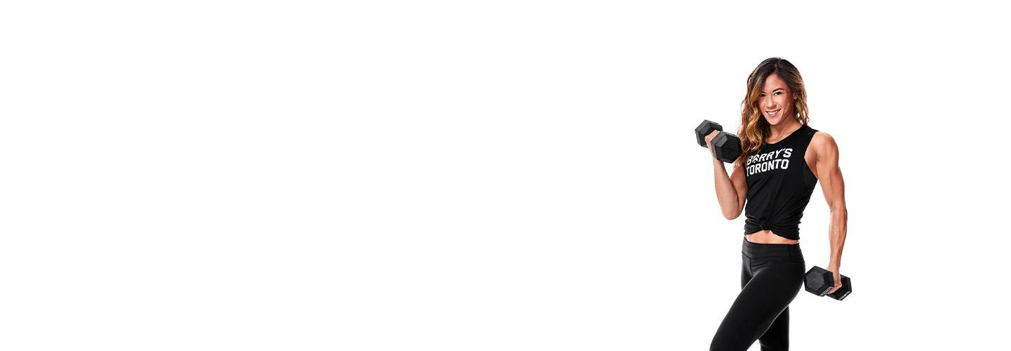 Instructor Michelle Leung in black Barry's Bootcamp tank top smiling while holding dumbbells on white background