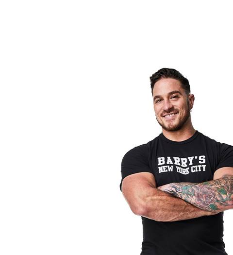 Barry’s instructor wearing a black top standing confidently smiling against a white background