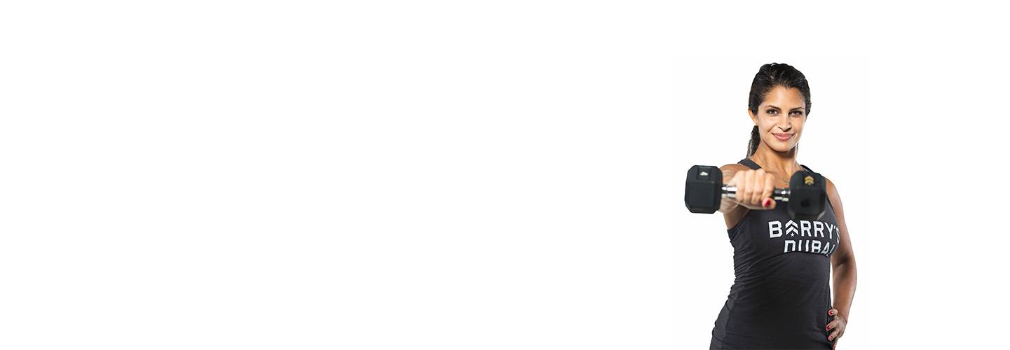 Instructor Nourie Mansour in black Barry's Bootcamp tank top holding dumbbell out in front on white background