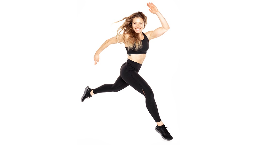 Barry's Bootcamp instructor Giorgi leaping in a black sports bra and leggings against a white background.