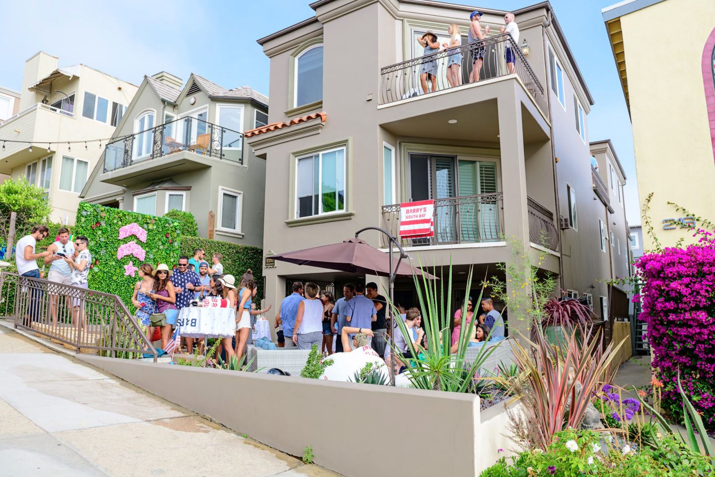 Rassemblement à l'événement Barry's Beach House vu de la rue avec logo floral rose et mur vivant visible sur le patio