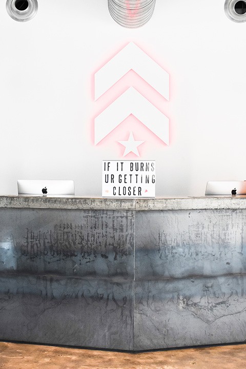 White Barry's Bootcamp upward arrows and star logo with red backlighting on white wall behind reception desk at Dubai DIFC studio location