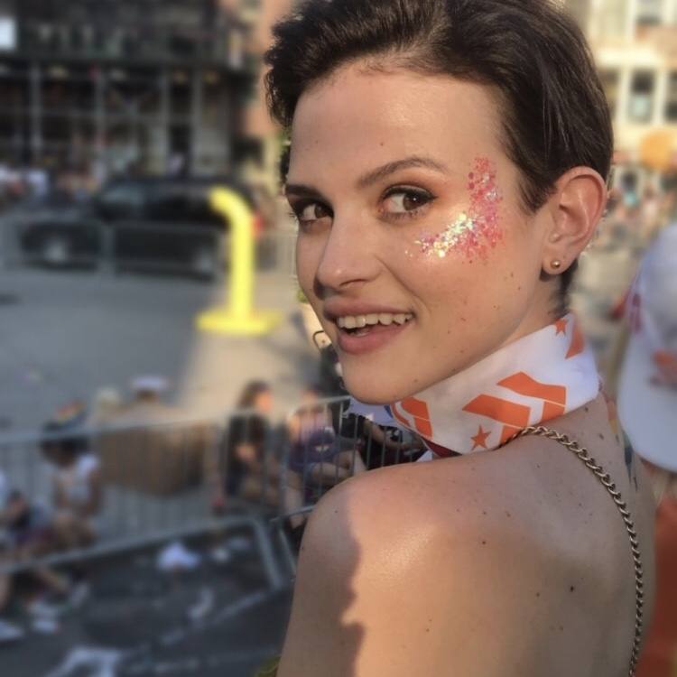 Young woman wearing Barry's Bootcamp bandana around neck with pink glitter on her cheek in urban setting