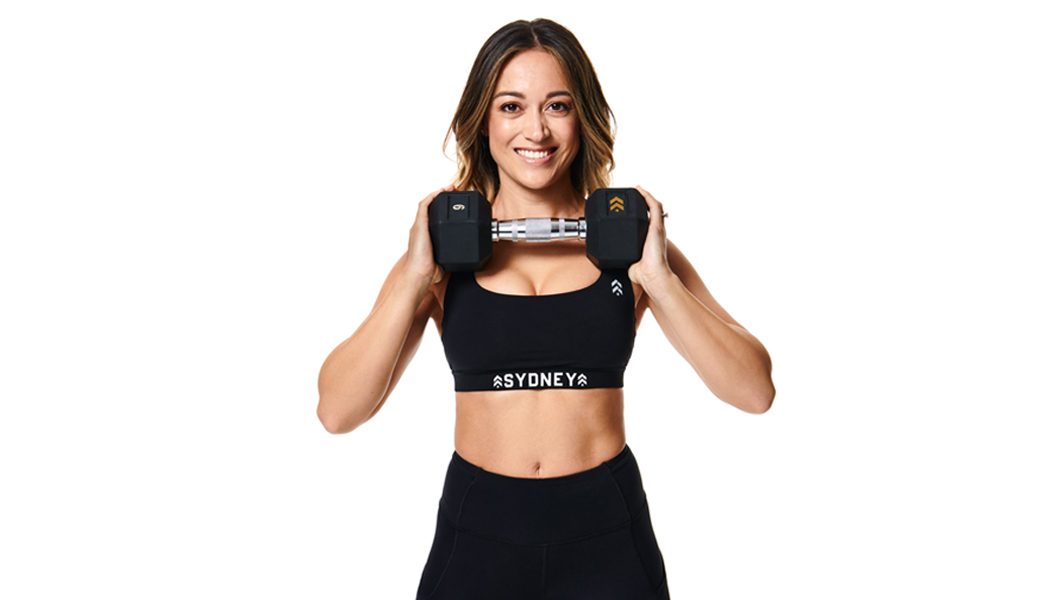 Instructor Joanne Boulat smiling while holding dumbbell with both hands underneath her chin