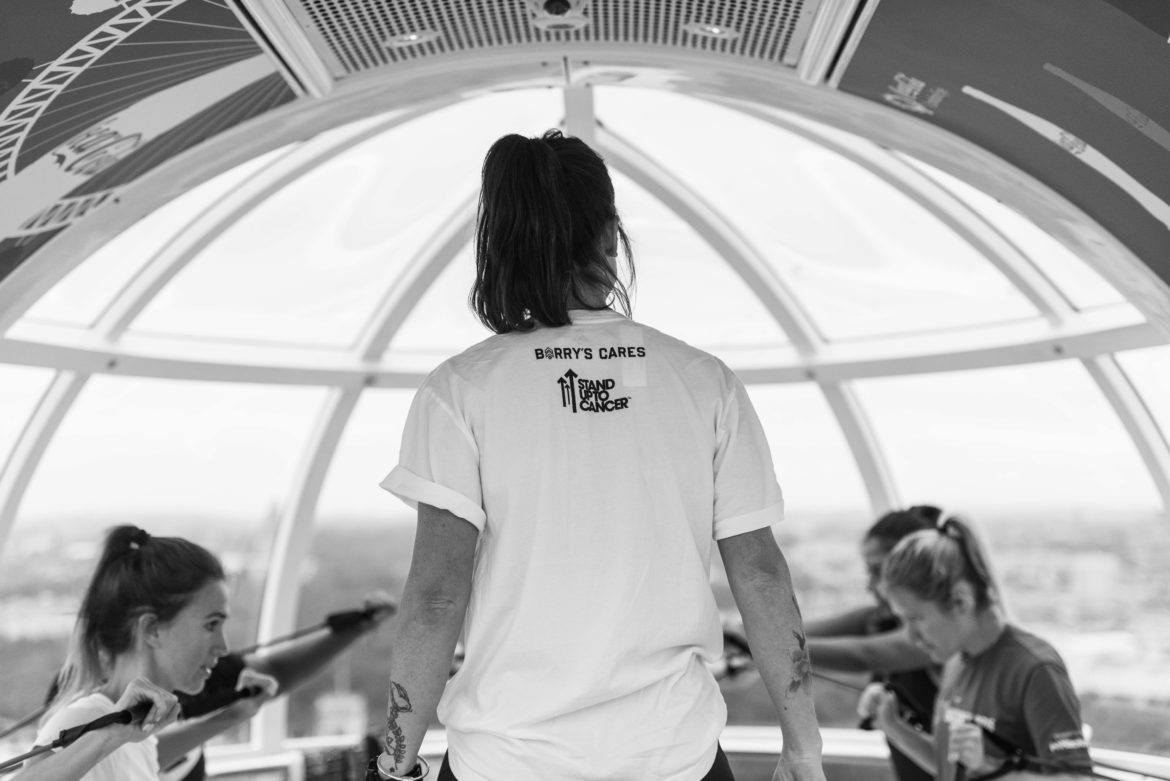 Baksidan av den kvinnliga Barry's Bootcamp-instruktören bär vit t-shirt när hon tittar på klassen i London Eye