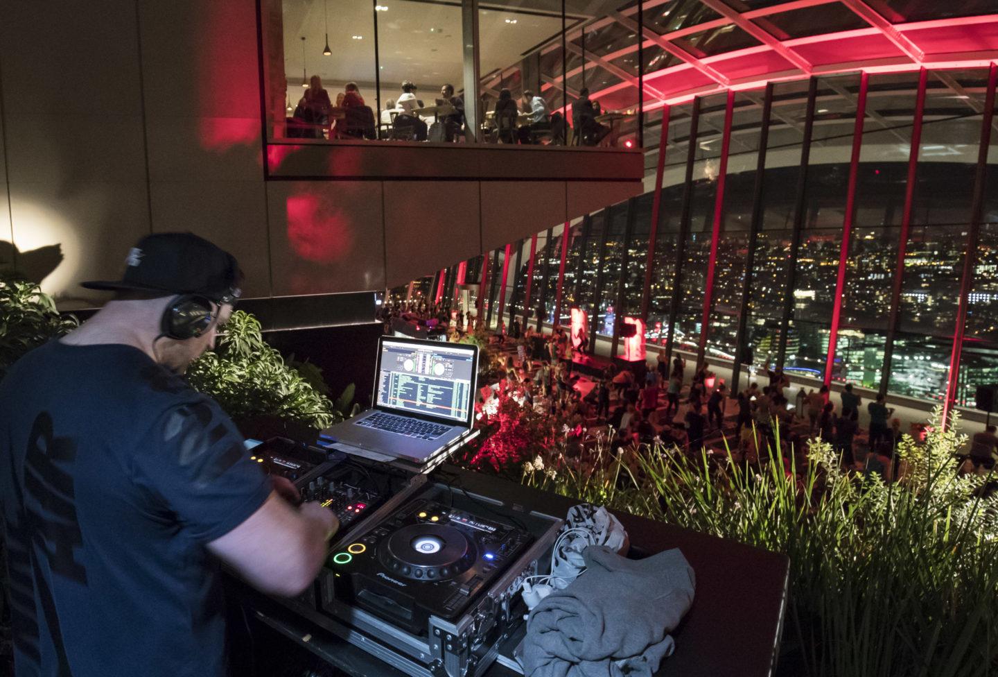 DJ overlooking Barry's Bootcamp nighttime fitness class in the London Sky Garden in front of large glass windows