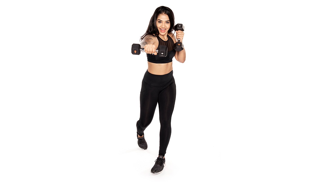 Barry's Bootcamp instructor Trishala Poulose wearing a black sports bra and leggings, making a punching motion with dumbbells.