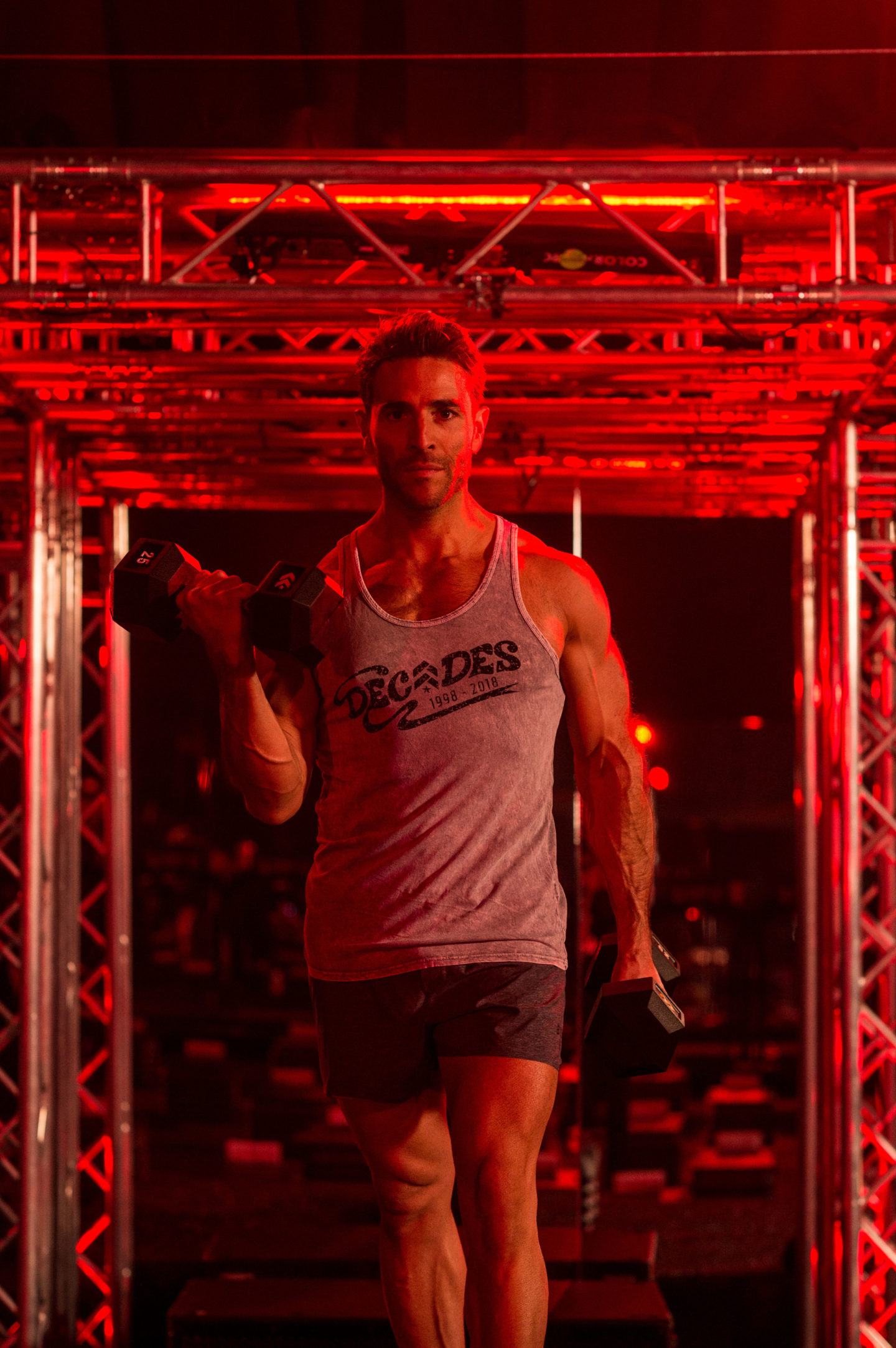 L'instructeur masculin de Barry's Bootcamp portant un débardeur gris de plusieurs décennies Red Room faire des flexions des biceps avec des haltères