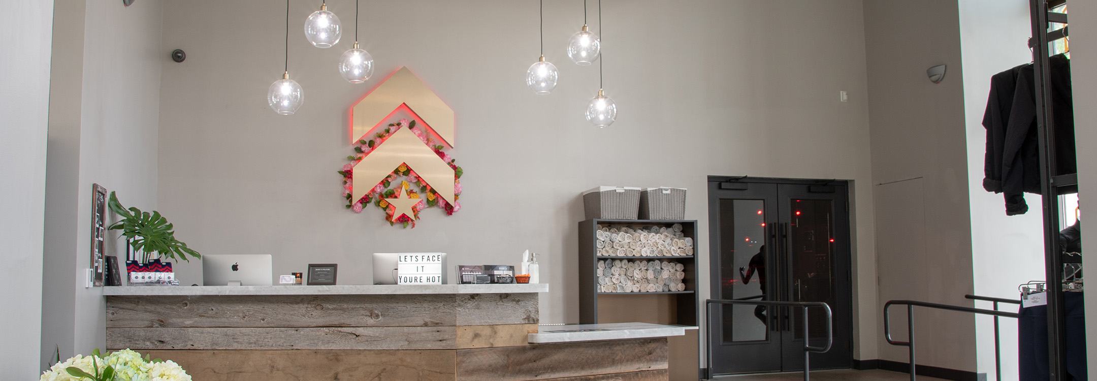 White Barry's Bootcamp upward arrows and star logo with colorful background on white wall behind reception desk at Atlanta studio location