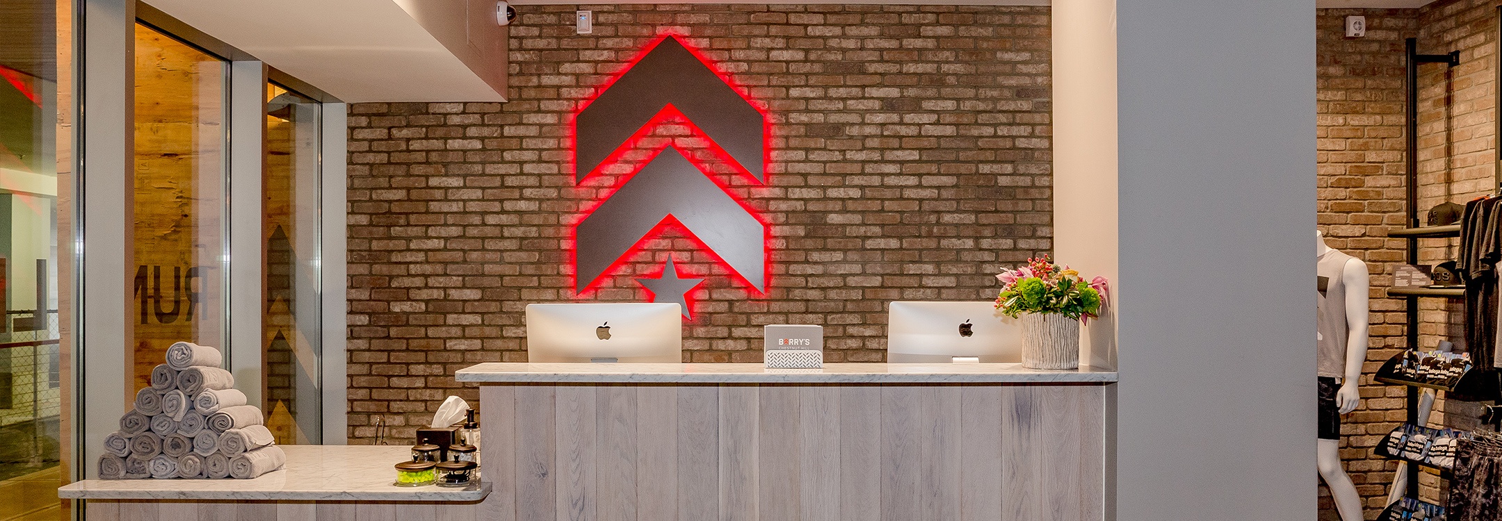 Silver Barry's Bootcamp upward arrows and star logo with red backlighting on wall behind reception desk at Chestnut Hill studio location