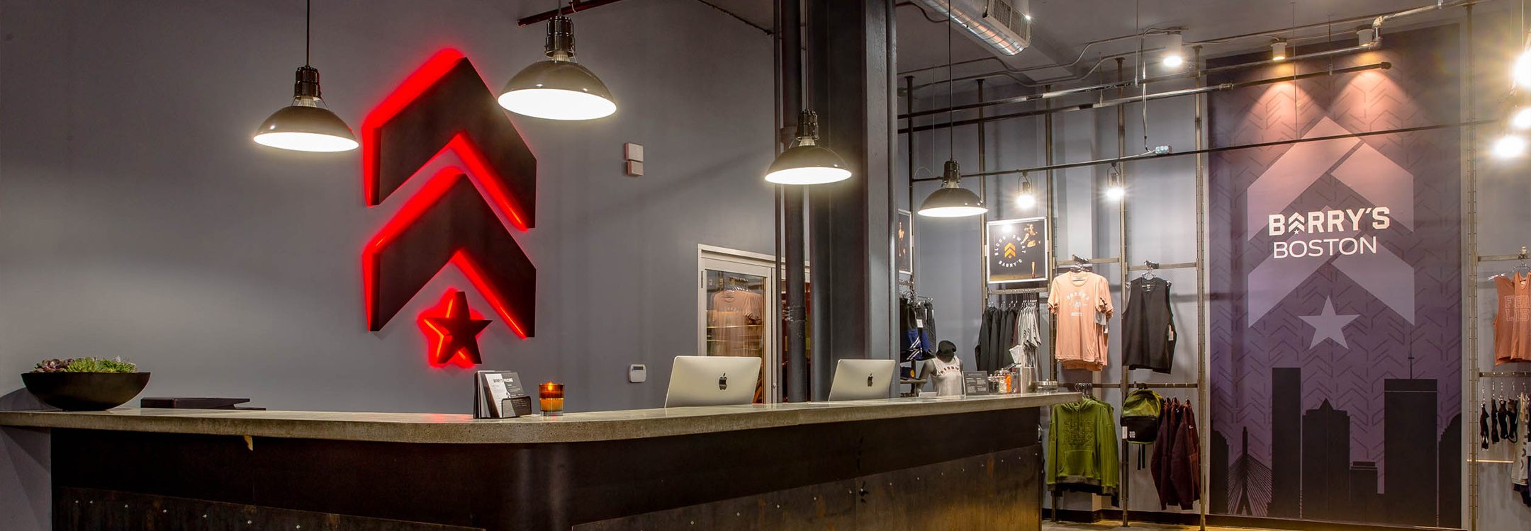 Grey Barry's Bootcamp upward arrows and star logo with red backlighting on wall behind reception desk at Downtown Boston studio location