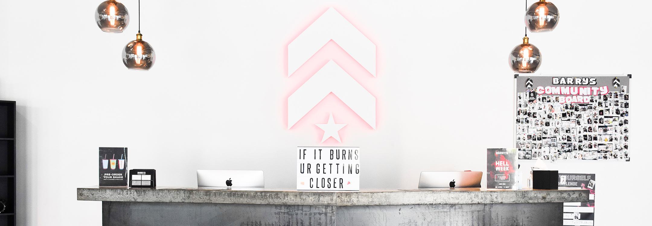 White Barry's Bootcamp upward arrows and star logo with red backlighting on white wall behind reception desk at Dubai DIFC studio location