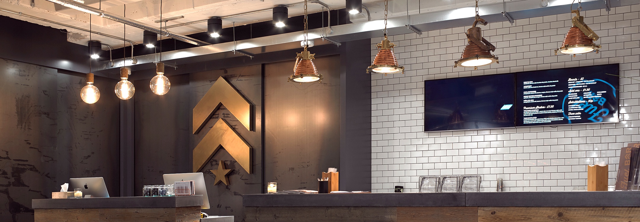 Gold Barry's Bootcamp upward arrows and star logo on wall behind reception desk at London West studio location