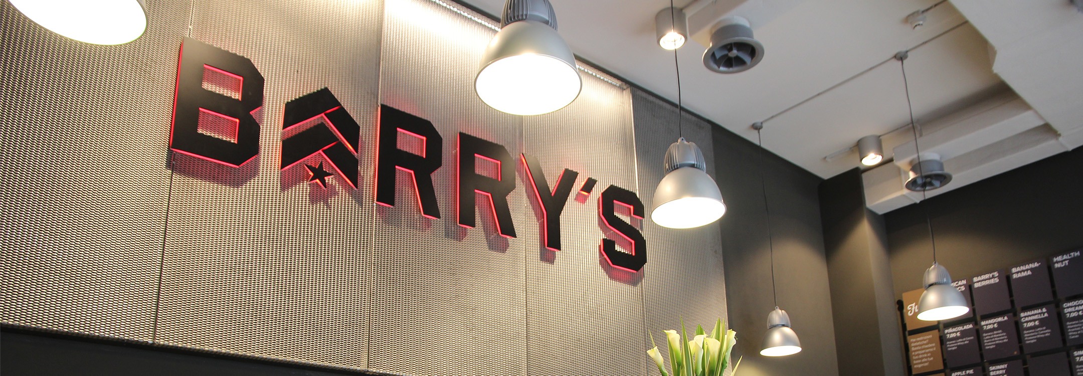 Grey Barry's Bootcamp sign with red backlighting on wall behind reception desk at Milan studio location