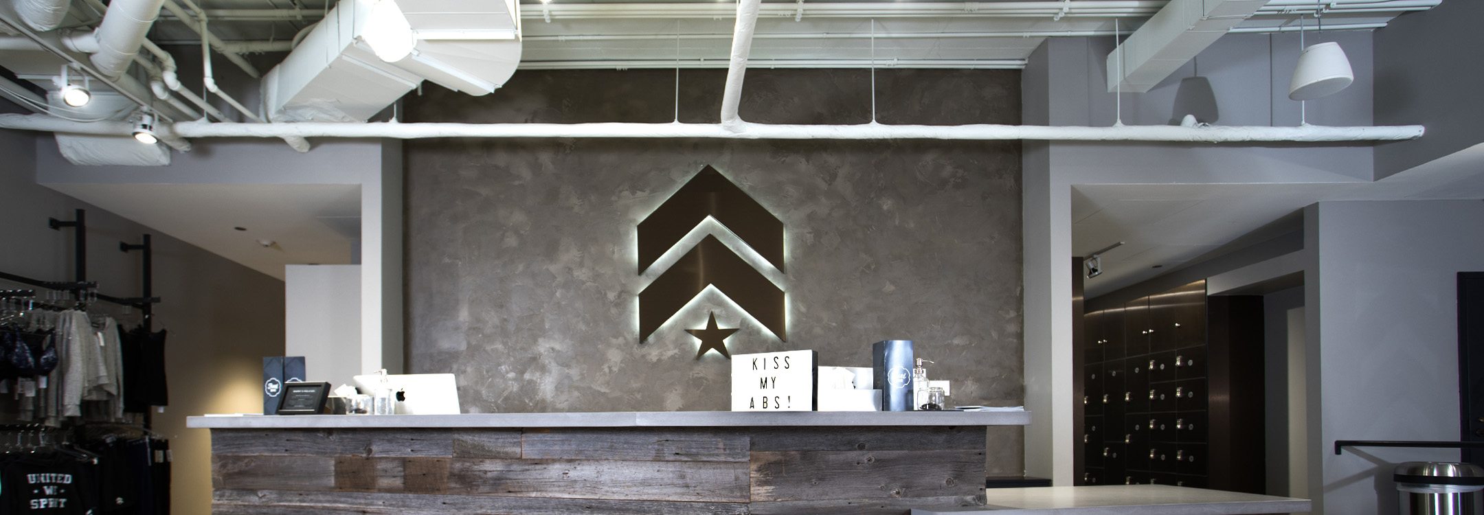 Grey Barry's Bootcamp upward arrows and star logo with white backlighting on wall behind reception desk at Richmond studio location