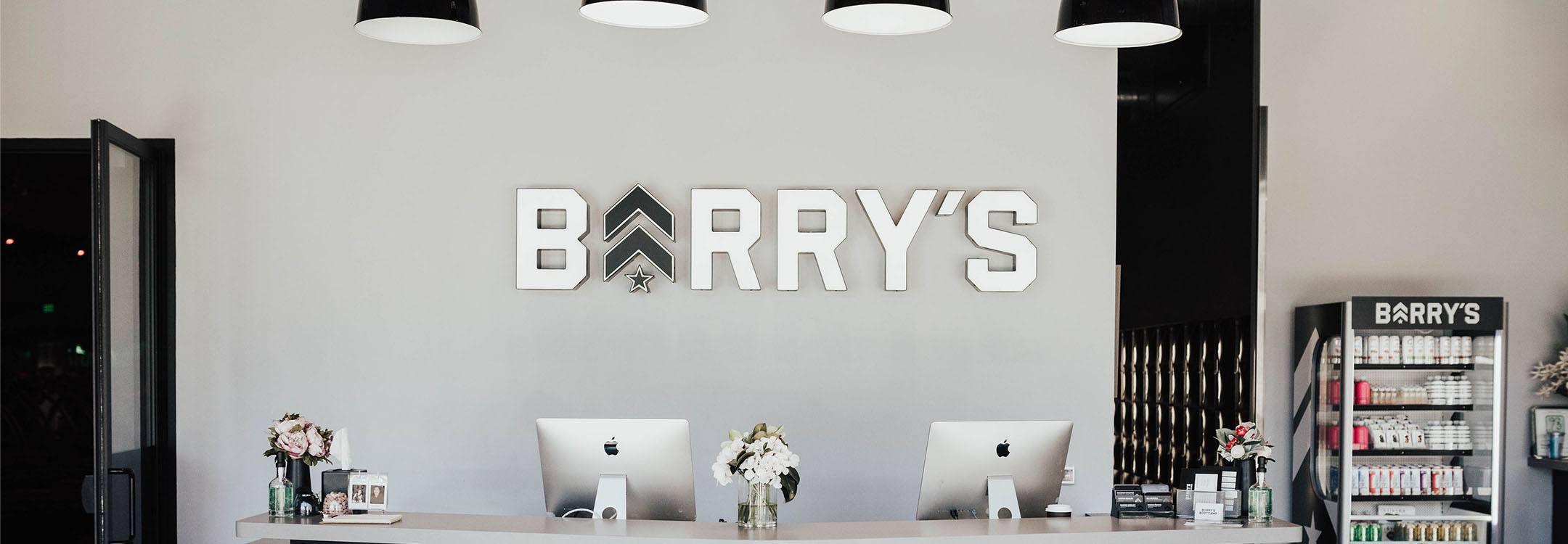 White Barry's Bootcamp sign and grey logo on white wall behind reception desk at San Fransisco studio location