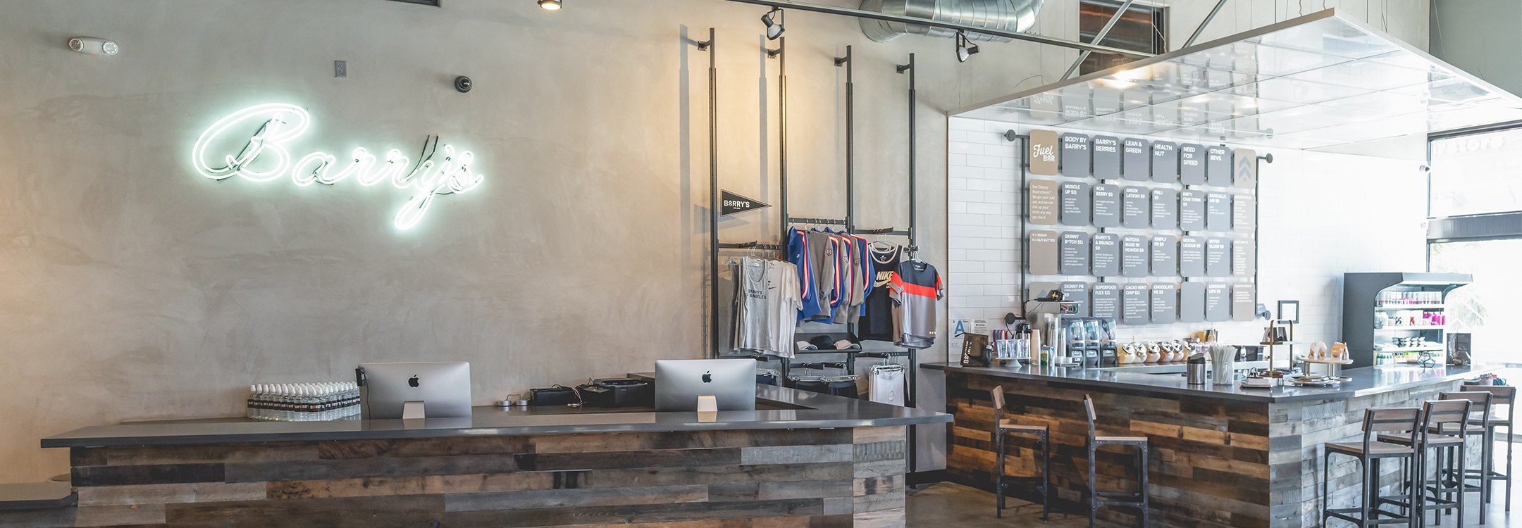 Cursive neon Barry's sign on wall behind clothing racks and reception area at Venice studio location