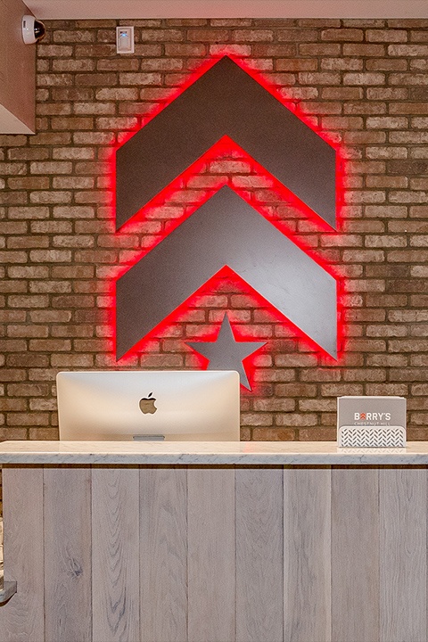Silver Barry's Bootcamp upward arrows and star logo with red backlighting on wall behind reception desk at Chestnut Hill studio location