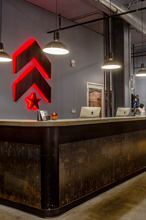 Grey Barry's Bootcamp upward arrows and star logo with red backlighting on wall behind reception desk at Downtown Boston studio location