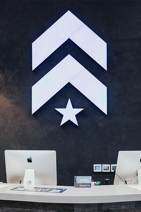 White Barry's Bootcamp upward arrows and star logo on navy wall behind reception desk at FiDi studio location