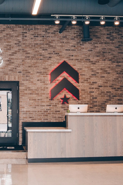 Grey Barry's Bootcamp upward arrows and star logo with red backlighting on wall behind reception desk at Lincoln Park studio location