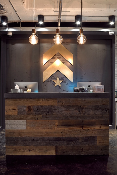 Gold Barry's Bootcamp upward arrows and star logo on wall behind reception desk at London West studio location
