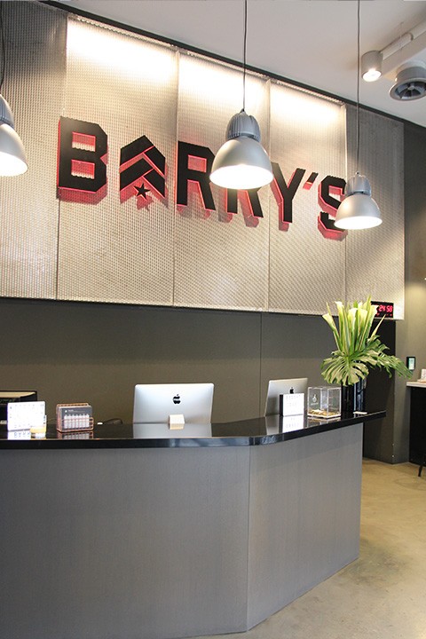 Grey Barry's Bootcamp sign with red backlighting on wall behind reception desk at Milan studio location