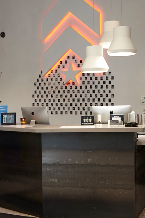White Barry's Bootcamp upward arrows and star logo with red backlighting on wall behind reception desk at Park Ave South studio location