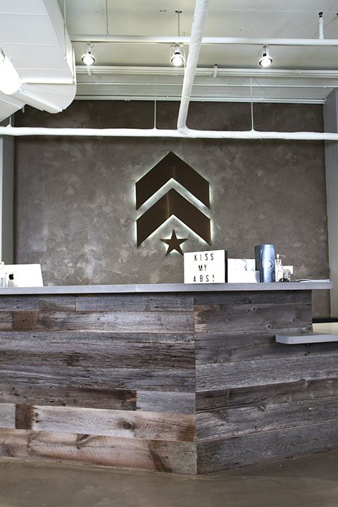 Grey Barry's Bootcamp upward arrows and star logo with white backlighting on wall behind reception desk at Richmond studio location