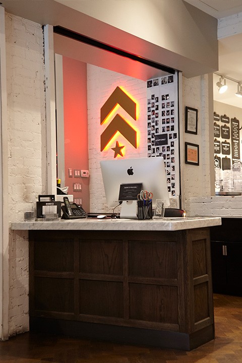 Gold Barry's Bootcamp upward arrows and star logo with red backlighting on white wall behind reception desk at Upper West Side studio location