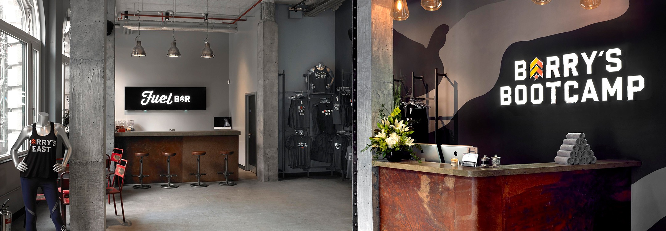 Barry's Bootcamp white sign and yellow and orange logo on wall behind reception desk at London East studio location