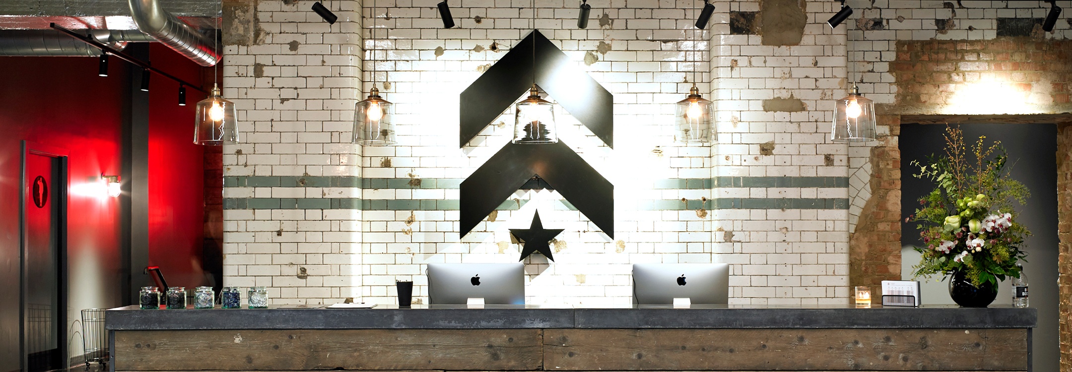 Black Barry's Bootcamp upward arrows and star logo on white tile wall behind reception desk at London SW1 studio location