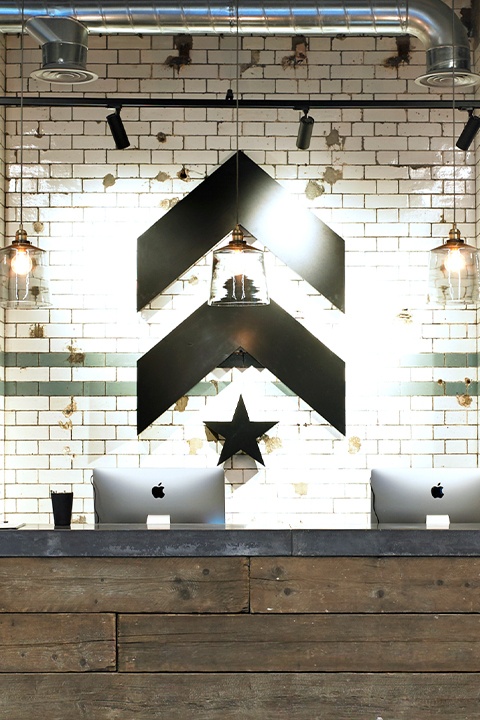 Black Barry's Bootcamp upward arrows and star logo on white tile wall behind reception desk at London SW1 studio location