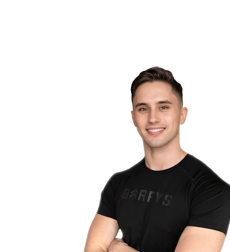 Barry’s instructor wearing a black top standing confidently smiling against a white background