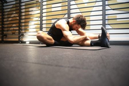 Hombre estirando su tendón de la corva en una estera de yoga negra