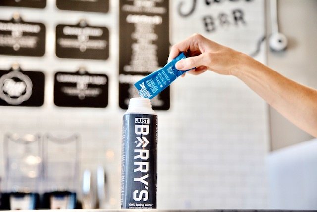 Persona vertiendo polvo de péptidos de colágeno de proteínas vitales en una botella de agua JUST