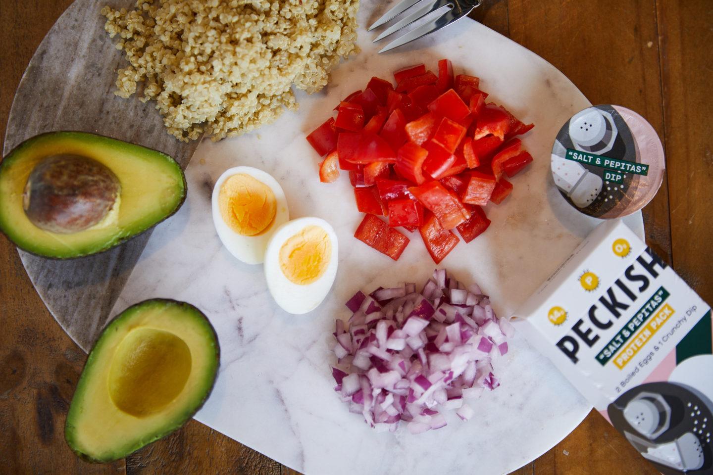 Tabla de cortar con aguacate, huevos cocidos, quinua, cebolla roja y tomate